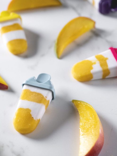 Ghiaccioli cocco e mango a strati bianchi e gialli, circondati da spicchi di mango fresco