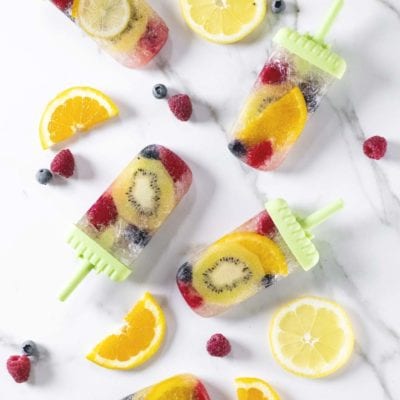 Ghiaccioli con frutta e prosecco con kiwi, arancia, lamponi e mirtilli interi nel ghiaccio