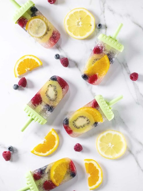 Ghiaccioli con frutta e prosecco con kiwi, arancia, lamponi e mirtilli interi nel ghiaccio