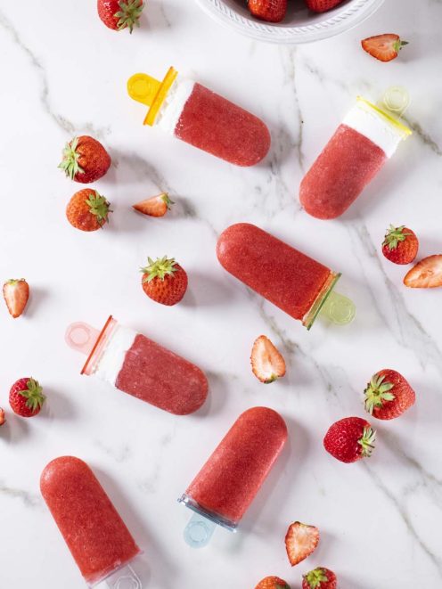 Ghiaccioli panna e fragole disposti con fragole fresche intere e a fette