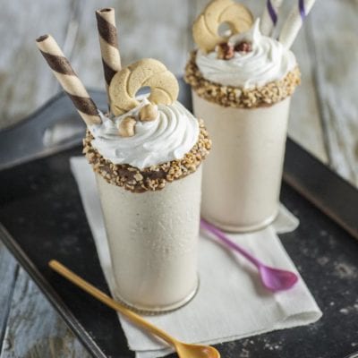 Milkshake alla nocciola con panna montata, granella di nocciole sul bordo e cialde arrotolate