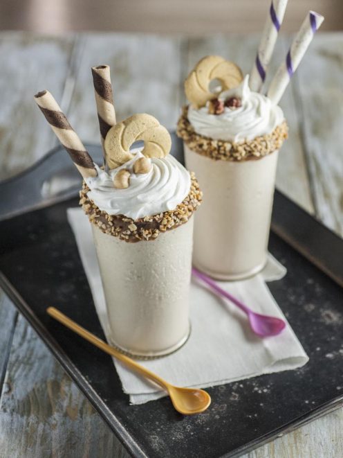 Milkshake alla nocciola con panna montata, granella di nocciole sul bordo e cialde arrotolate