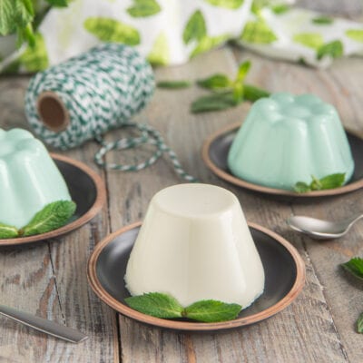 Pannacotta alla menta sformata, una bianca e due verde menta, guarnite con foglie di menta fresca