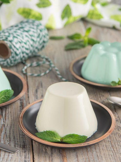 Pannacotta alla menta sformata, una bianca e due verde menta, guarnite con foglie di menta fresca