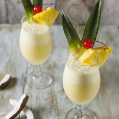 Piña colada cremosa guarnita con fetta di ananas, foglie e ciliegia al maraschino