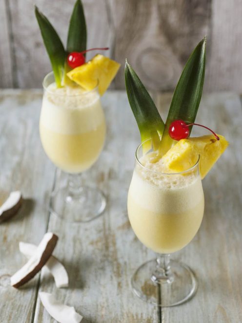 Piña colada cremosa guarnita con fetta di ananas, foglie e ciliegia al maraschino