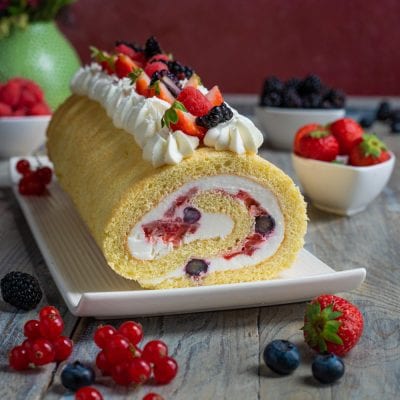 Rotolo con panna e frutti di bosco farcito, con fragole, mirtilli e more in cima