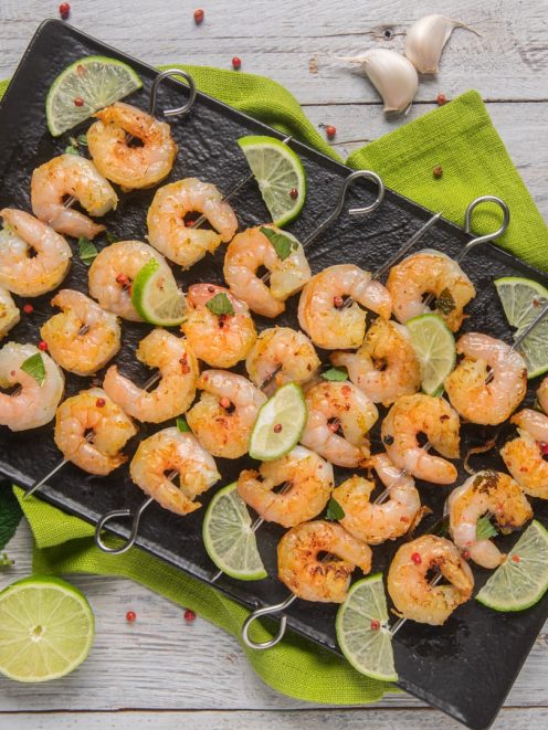 Spiedini di gamberi grigliati con fettine di lime e pepe rosa