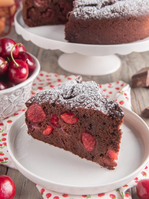 Torta al cioccolato e ciliegie in fetta, con le ciliegie visibili nell'impasto e zucchero a velo