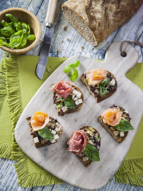 Bruschette con radicchio guarnite con salmone affumicato, salame e foglie di basilico fresco