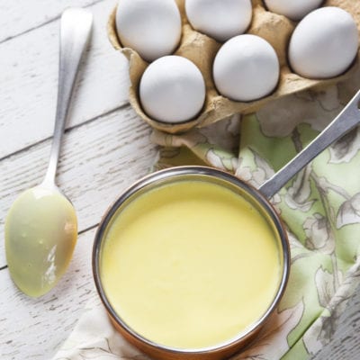 Crema inglese liscia e vellutata in una casseruola, con uova fresche sullo sfondo