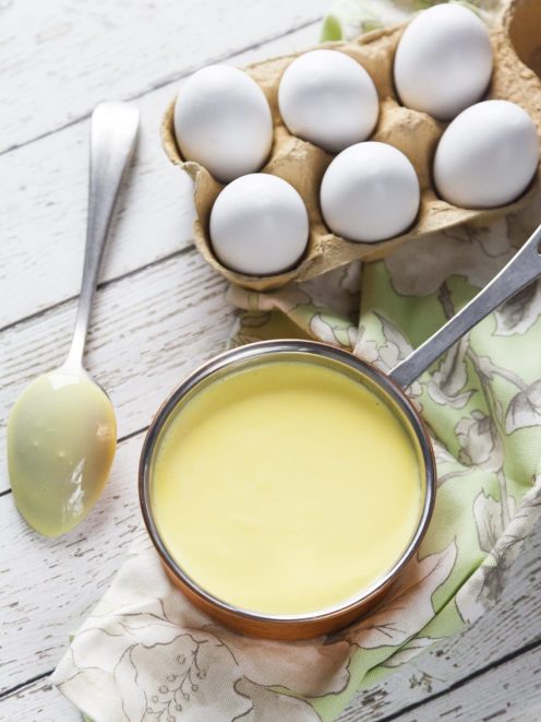 Crema inglese liscia e vellutata in una casseruola, con uova fresche sullo sfondo