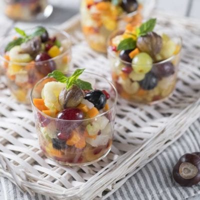 Macedonia autunnale servita in bicchieri con uva, castagne, frutta a pezzi e foglie di menta fresca