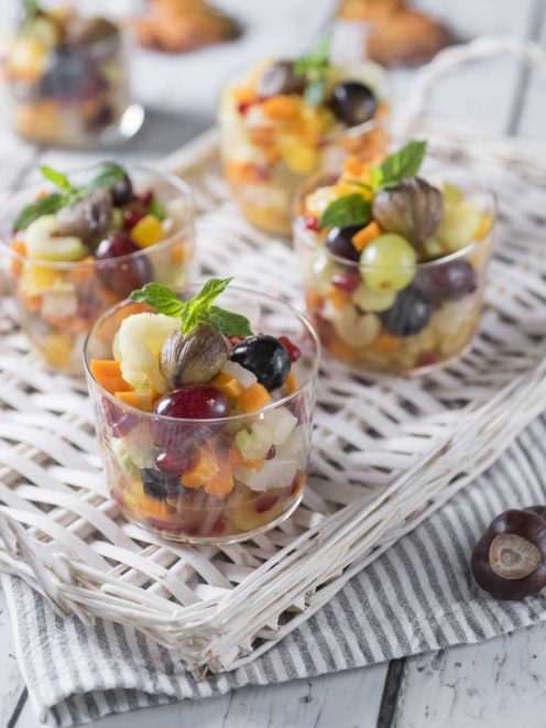 Macedonia autunnale servita in bicchieri con uva, castagne, frutta a pezzi e foglie di menta fresca