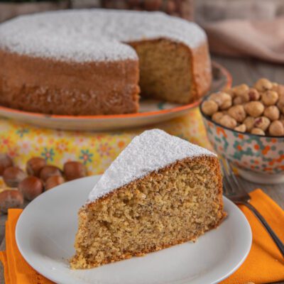 Torta di nocciole con una fetta in primo piano spolverata di zucchero a velo