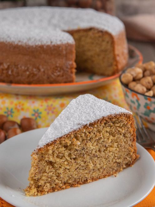 Torta di nocciole con una fetta in primo piano spolverata di zucchero a velo