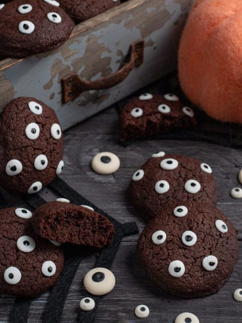 Biscotti di Halloween al cacao decorati con occhietti di zucchero, uno spezzato mostra l'interno morbido