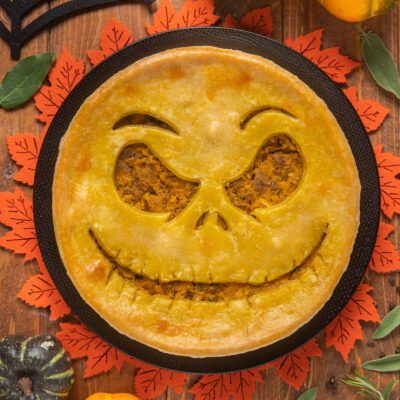 Pie salata di Halloween con sfoglia dorata e ripieno di zucca, decorata con una faccia jack-o'-lantern