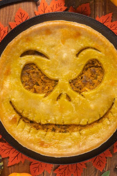 Pie salata di Halloween con sfoglia dorata e ripieno di zucca, decorata con una faccia jack-o'-lantern