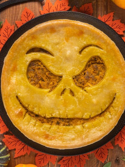 Pie salata di Halloween con sfoglia dorata e ripieno di zucca, decorata con una faccia jack-o'-lantern