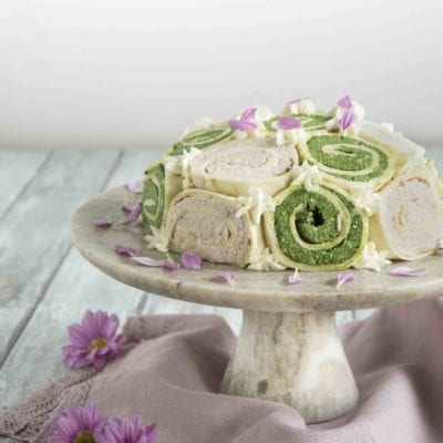 Zuccotto di piadina con rotoli verdi agli spinaci e rosa, decorato con ciuffi di crema e petali eduli