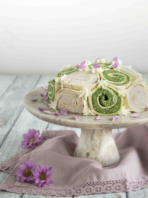Zuccotto di piadina con rotoli verdi agli spinaci e rosa, decorato con ciuffi di crema e petali eduli