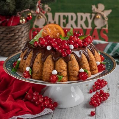 Budino di panettone glassato al cioccolato, guarnito con ribes rosso, fettina d'arancia e foglie di menta