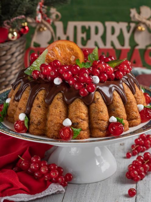 Budino di panettone glassato al cioccolato, guarnito con ribes rosso, fettina d'arancia e foglie di menta