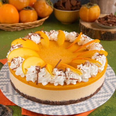 Cheesecake ai cachi con gelatina arancione, fettine di frutto fresco, ciuffi di panna e scaglie di cioccolato