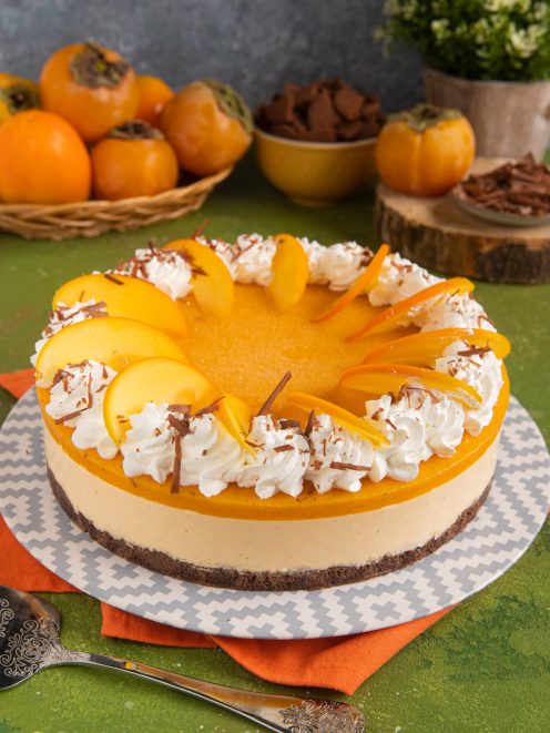 Cheesecake ai cachi con gelatina arancione, fettine di frutto fresco, ciuffi di panna e scaglie di cioccolato