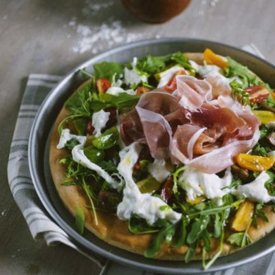 Focaccia senza glutine con rucola fresca, stracciatella, prosciutto crudo e verdure colorate