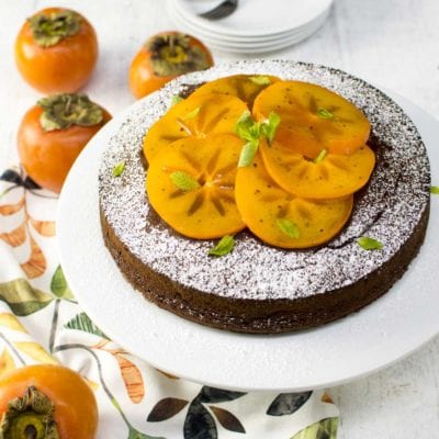 Torta ai cachi e cioccolato spolverata di zucchero a velo, guarnita con fette di cachi e foglioline di menta