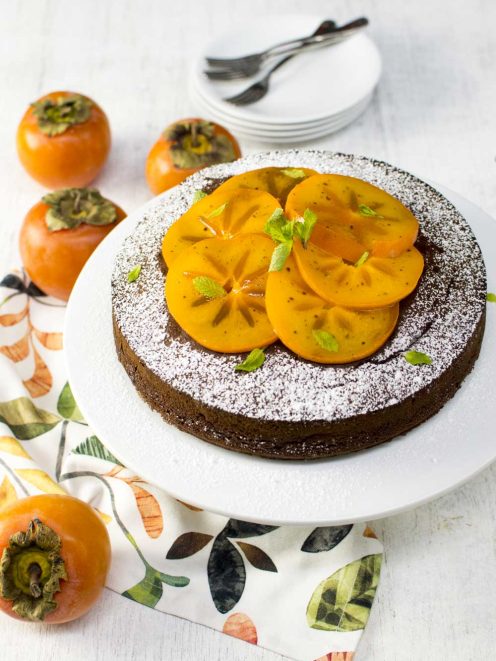 Torta ai cachi e cioccolato spolverata di zucchero a velo, guarnita con fette di cachi e foglioline di menta
