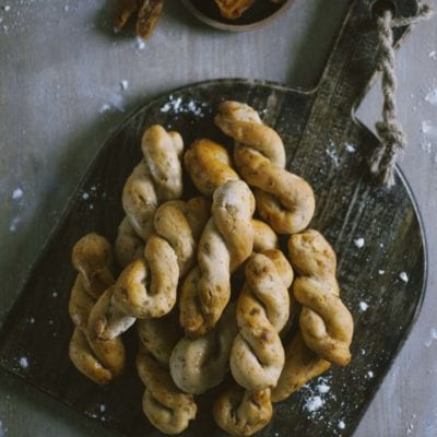 Treccine con fichi e noci impilate su tagliere, con fichi secchi sullo sfondo