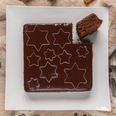 Torta fondente glassata al cioccolato con stelle dorate e argentate sulla superficie lucida, una fetta sollevata mostra l'interno soffice