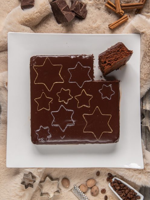 Torta fondente glassata al cioccolato con stelle dorate e argentate sulla superficie lucida, una fetta sollevata mostra l'interno soffice