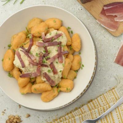 Gnocchi di patate dolci con crema di noci e listarelle di speck croccante, guarniti con erba cipollina