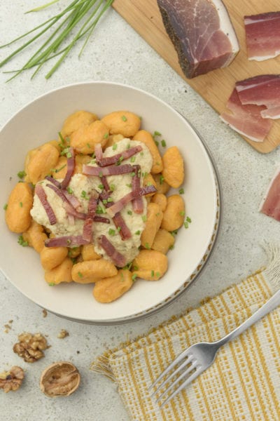 Gnocchi di patate dolci con crema di noci e listarelle di speck croccante, guarniti con erba cipollina