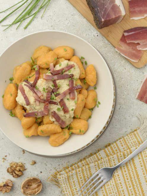 Gnocchi di patate dolci con crema di noci e listarelle di speck croccante, guarniti con erba cipollina