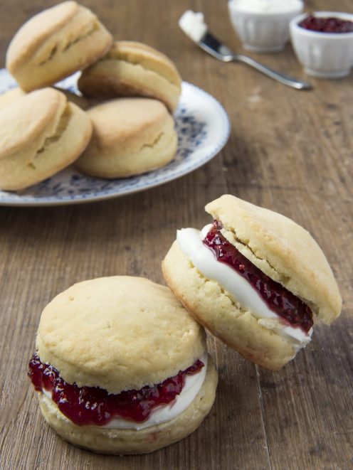 Scones farciti con crema e confettura di frutti rossi, serviti su un piano di legno