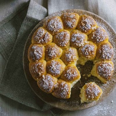 Danubio dolce con rotolini dorati spolverati di zucchero a velo e granella, con un pezzo staccato