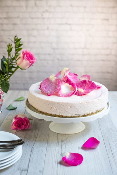 Cheesecake alle rose senza glutine con petali canditi sulla superficie e base di biscotti