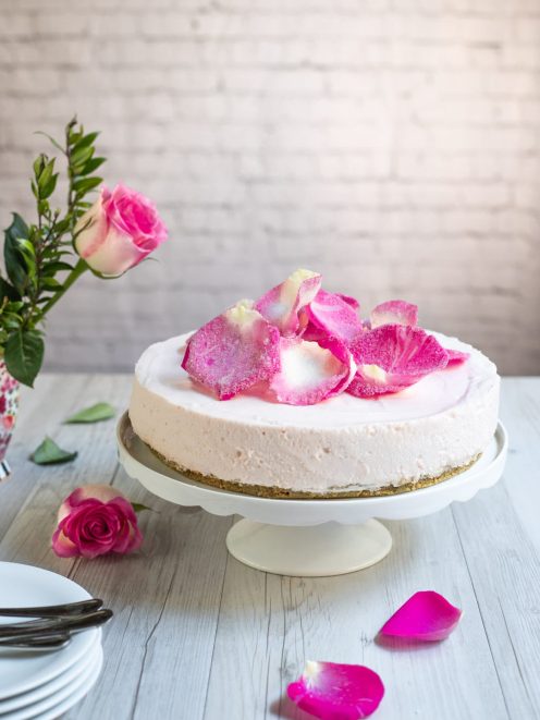 Cheesecake alle rose senza glutine con petali canditi sulla superficie e base di biscotti