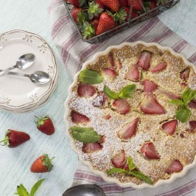 Clafoutis di fragole con fette di frutto affondato nella pastella, foglie di menta e zucchero a velo