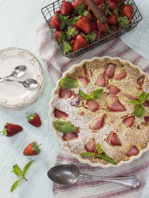 Clafoutis di fragole con fette di frutto affondato nella pastella, foglie di menta e zucchero a velo