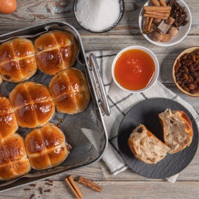Hot cross buns lucidi di glassa con croce, panetto tagliato a mostrare la mollica con uvetta e spezie