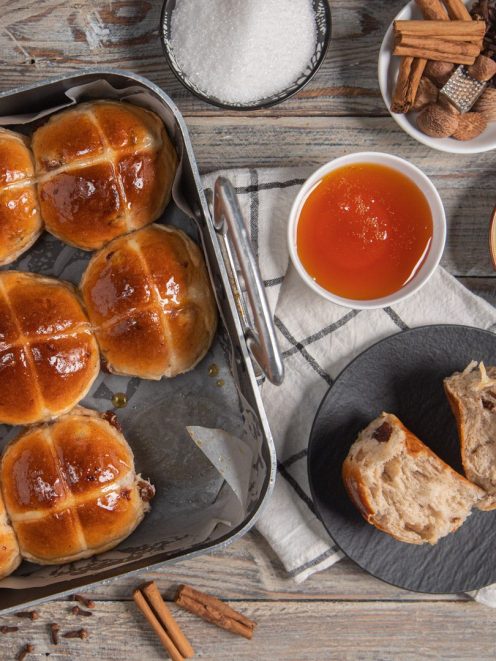 Hot cross buns lucidi di glassa con croce, panetto tagliato a mostrare la mollica con uvetta e spezie