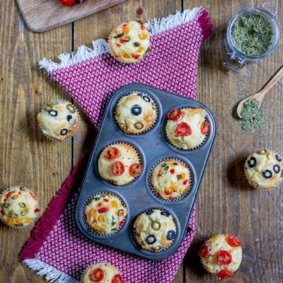 Muffin alle verdure appena sfornati con pomodorini, olive e peperoni colorati in superficie