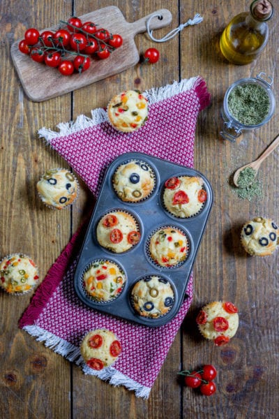 Muffin alle verdure appena sfornati con pomodorini, olive e peperoni colorati in superficie