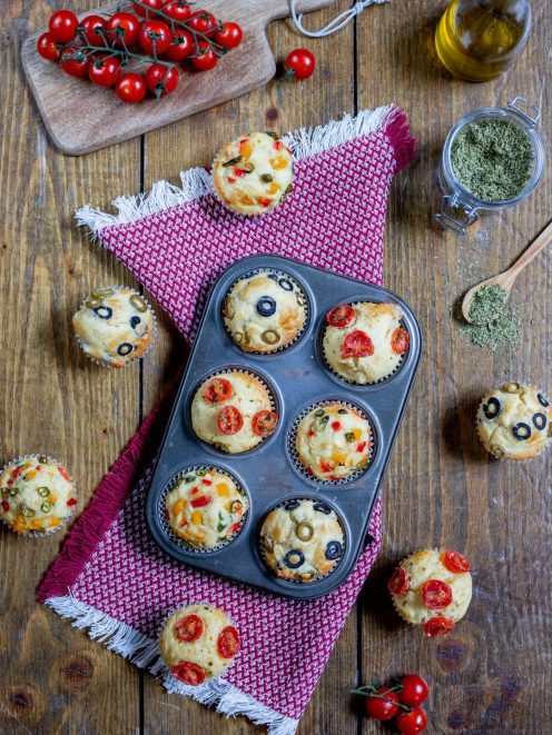 Muffin alle verdure appena sfornati con pomodorini, olive e peperoni colorati in superficie